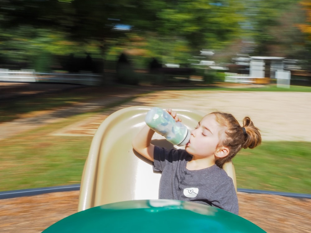 boy drinking from clear plastic bottle on blue plastic slide