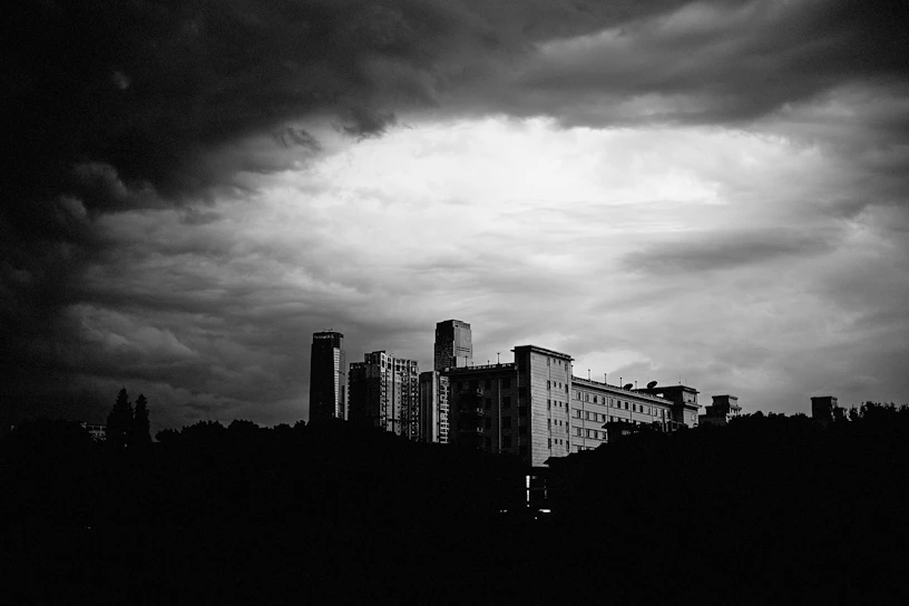 A striking black-and-white still from a cinematic narrative film, showcasing a dramatic silhouette against a moody urban backdrop.