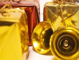Several decorative gift boxes are wrapped in shiny red and gold paper and adorned with golden strings. A couple of small golden bells are placed in front of the boxes, adding a festive touch.
