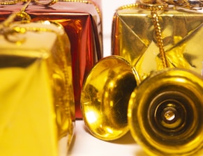 Several decorative gift boxes are wrapped in shiny red and gold paper and adorned with golden strings. A couple of small golden bells are placed in front of the boxes, adding a festive touch.