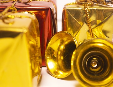 Several decorative gift boxes are wrapped in shiny red and gold paper and adorned with golden strings. A couple of small golden bells are placed in front of the boxes, adding a festive touch.
