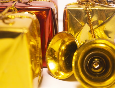 Several decorative gift boxes are wrapped in shiny red and gold paper and adorned with golden strings. A couple of small golden bells are placed in front of the boxes, adding a festive touch.