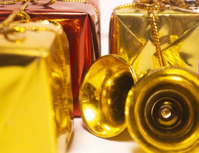 Several decorative gift boxes are wrapped in shiny red and gold paper and adorned with golden strings. A couple of small golden bells are placed in front of the boxes, adding a festive touch.