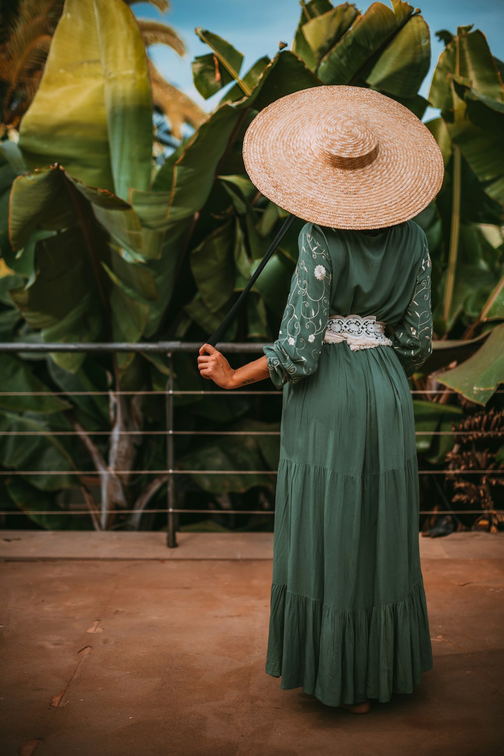 woman in green dress wearing brown straw hat standing near green leaf plant during daytime