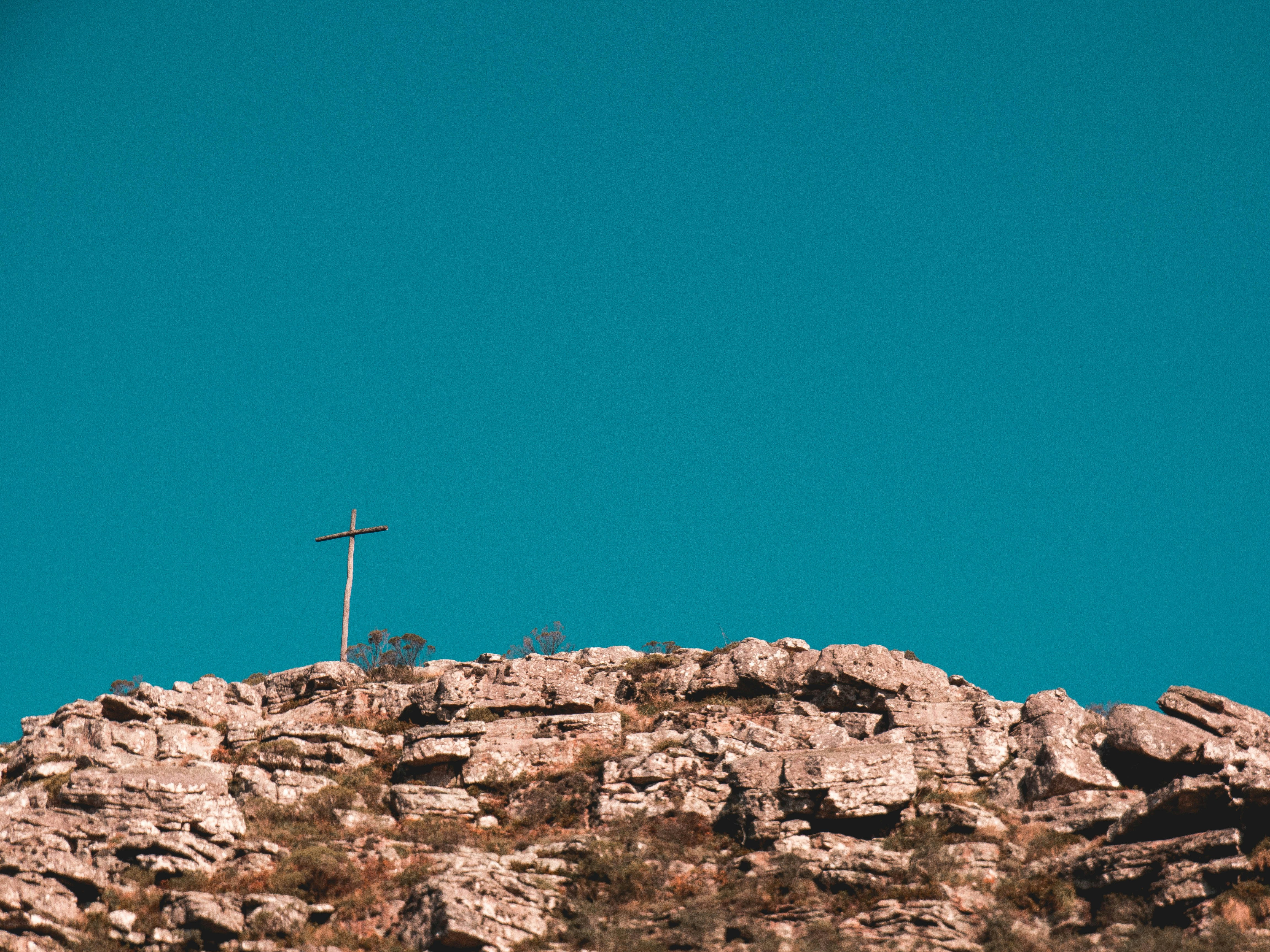cross on top of brown rock formation under blue sky during daytime