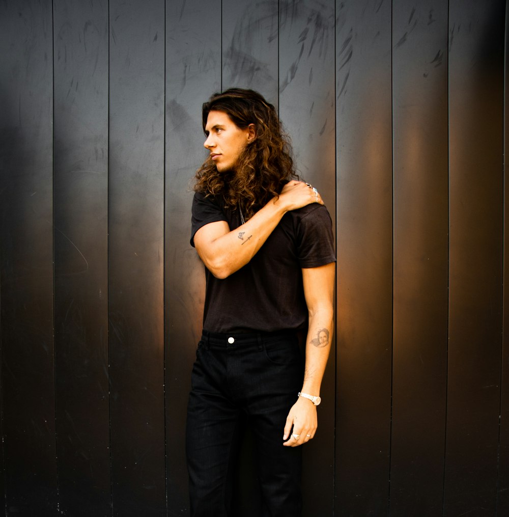 woman in black sleeveless shirt and black pants standing beside gray wall