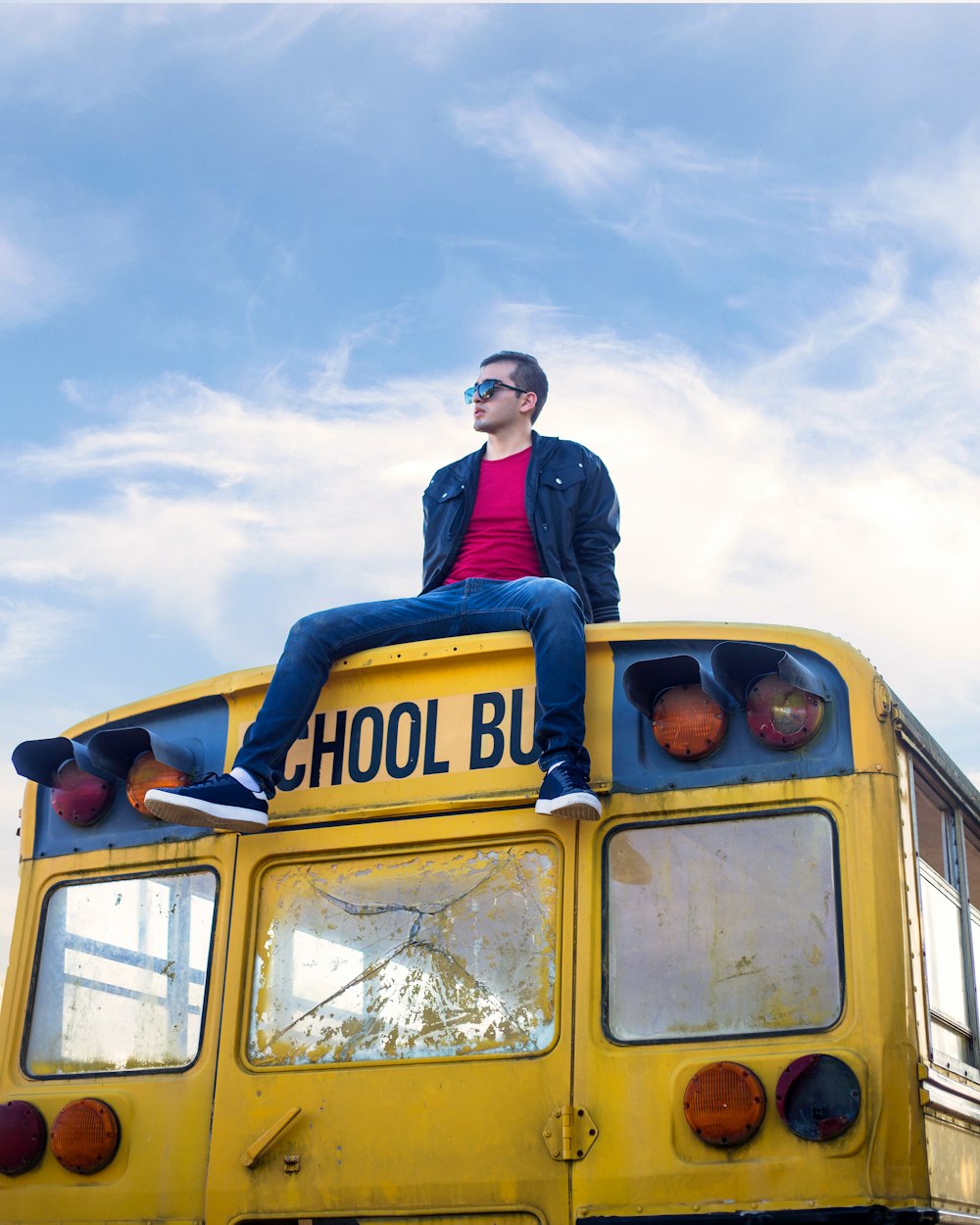 man in blue jacket standing beside yellow school bus under white clouds during daytime