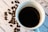 A steaming cup of coffee placed on a rustic wooden table with coffee beans scattered around.
