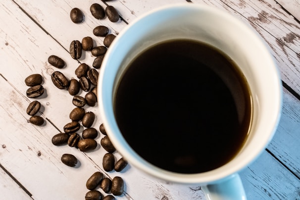 A steaming cup of black coffee on a wooden table with coffee beans scattered around.