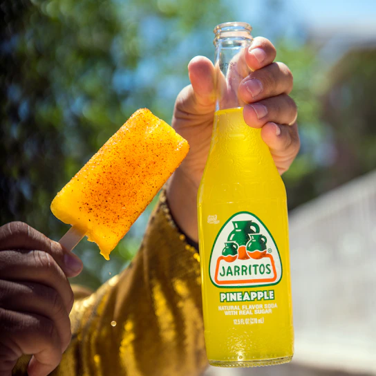 Hand holding a vibrant fruit paleta with a sunny outdoor background