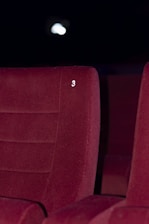 A red upholstered theater seat is prominently featured with the number three embossed on its backrest. The background is dimly lit, suggesting a cinema or theater environment.