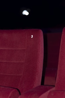 A red upholstered theater seat is prominently featured with the number three embossed on its backrest. The background is dimly lit, suggesting a cinema or theater environment.