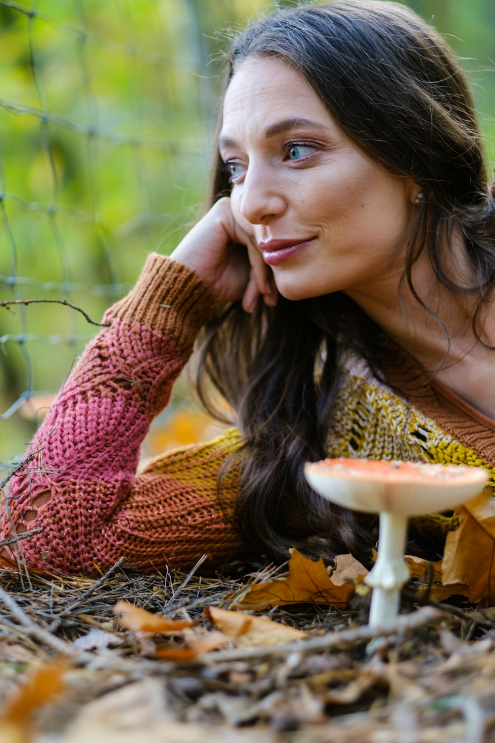 Frau im braunen Strickpullover liegt auf braunen getrockneten Blättern