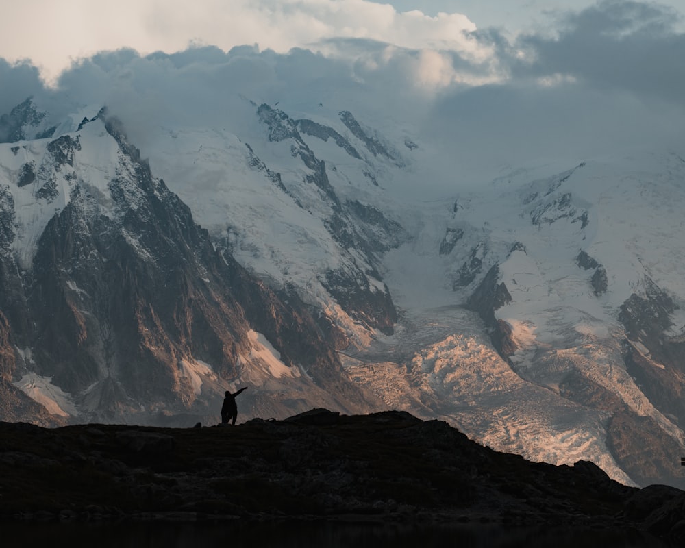 person standing on rock formation near snow covered mountain during daytime