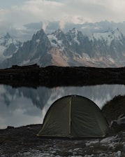 A rugged military tent pitched beside a peaceful Scandinavian lake at dawn.