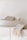 A white ceramic bowl containing folded beige and cream-colored towels. Another towel with fringed edges is draped over the edge of a minimalist white countertop.