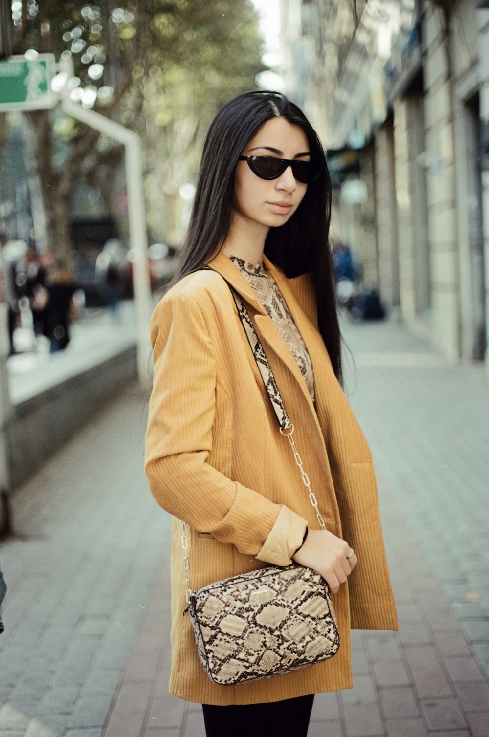 woman in orange blazer and black and white floral skirt wearing black sunglasses