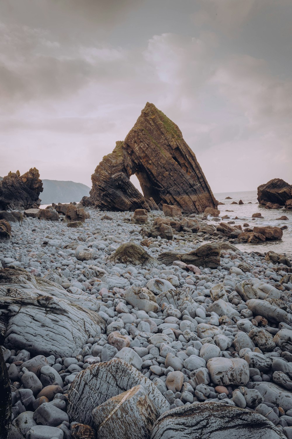 brown rock formation on body of water under cloudy sky during daytime