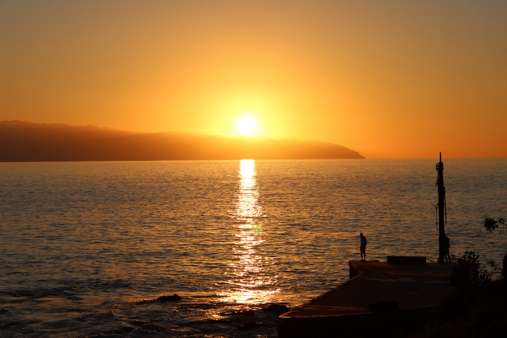 Silueta de la persona de pie en el muelle durante la puesta del sol