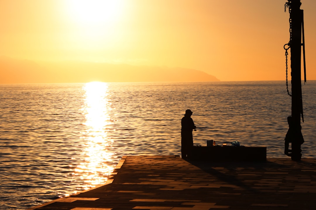 silhouette of man standing on dock during sunset