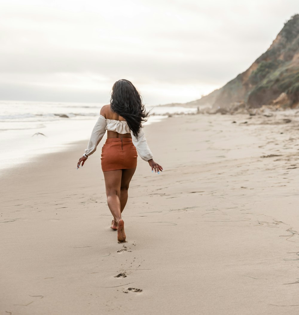 woman in white shirt walking on beach during daytime