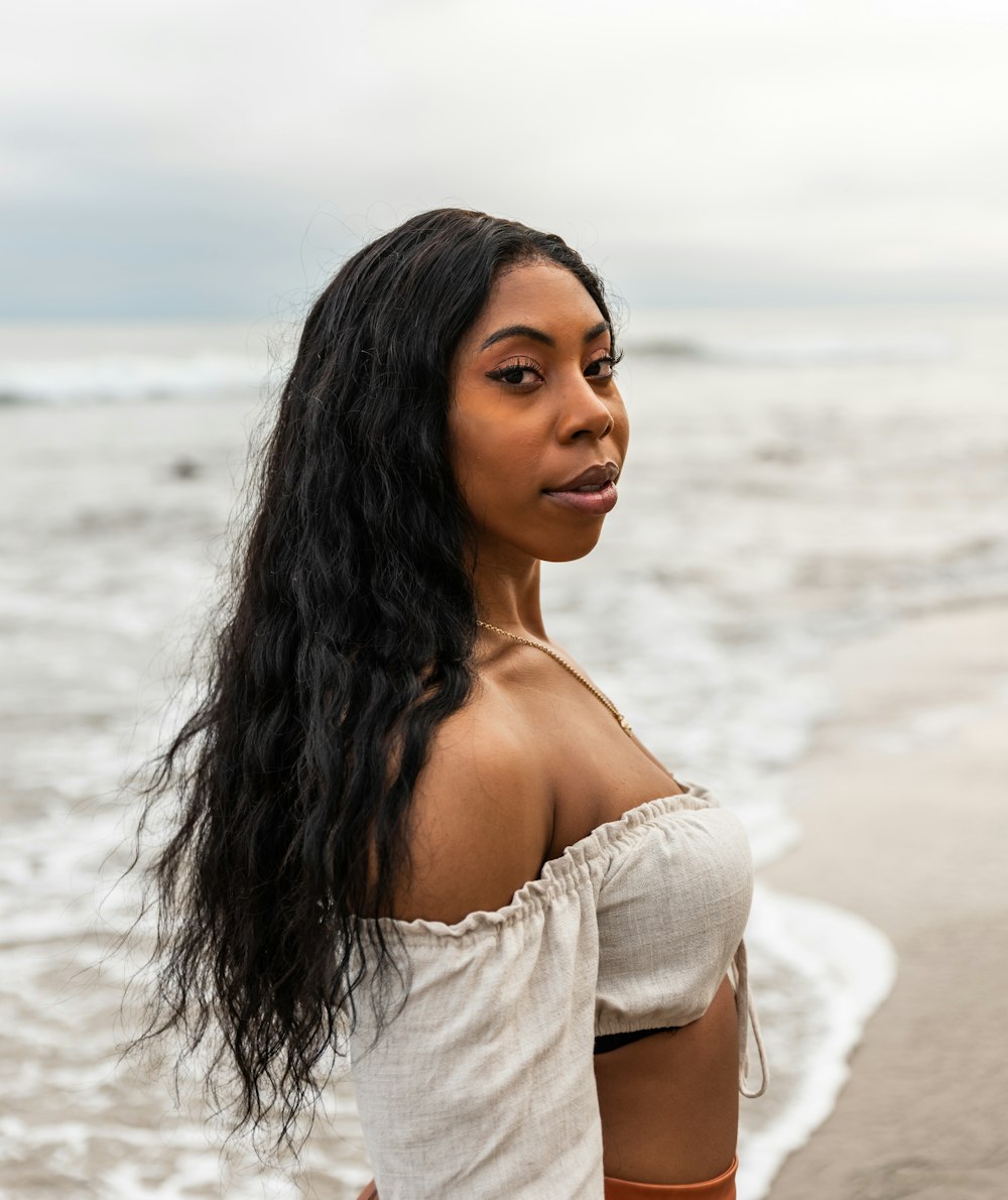 woman in white off shoulder shirt standing on beach during daytime