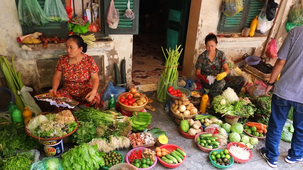 woman in red and white floral dress standing in front of vegetable stand