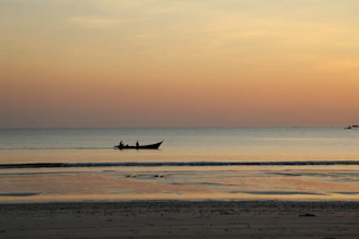 A serene beach scene at sunset, with a small boat anchored near the shore.