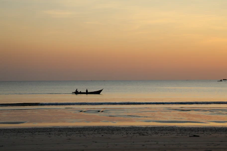 A serene beach scene at sunset, with a small boat anchored near the shore.