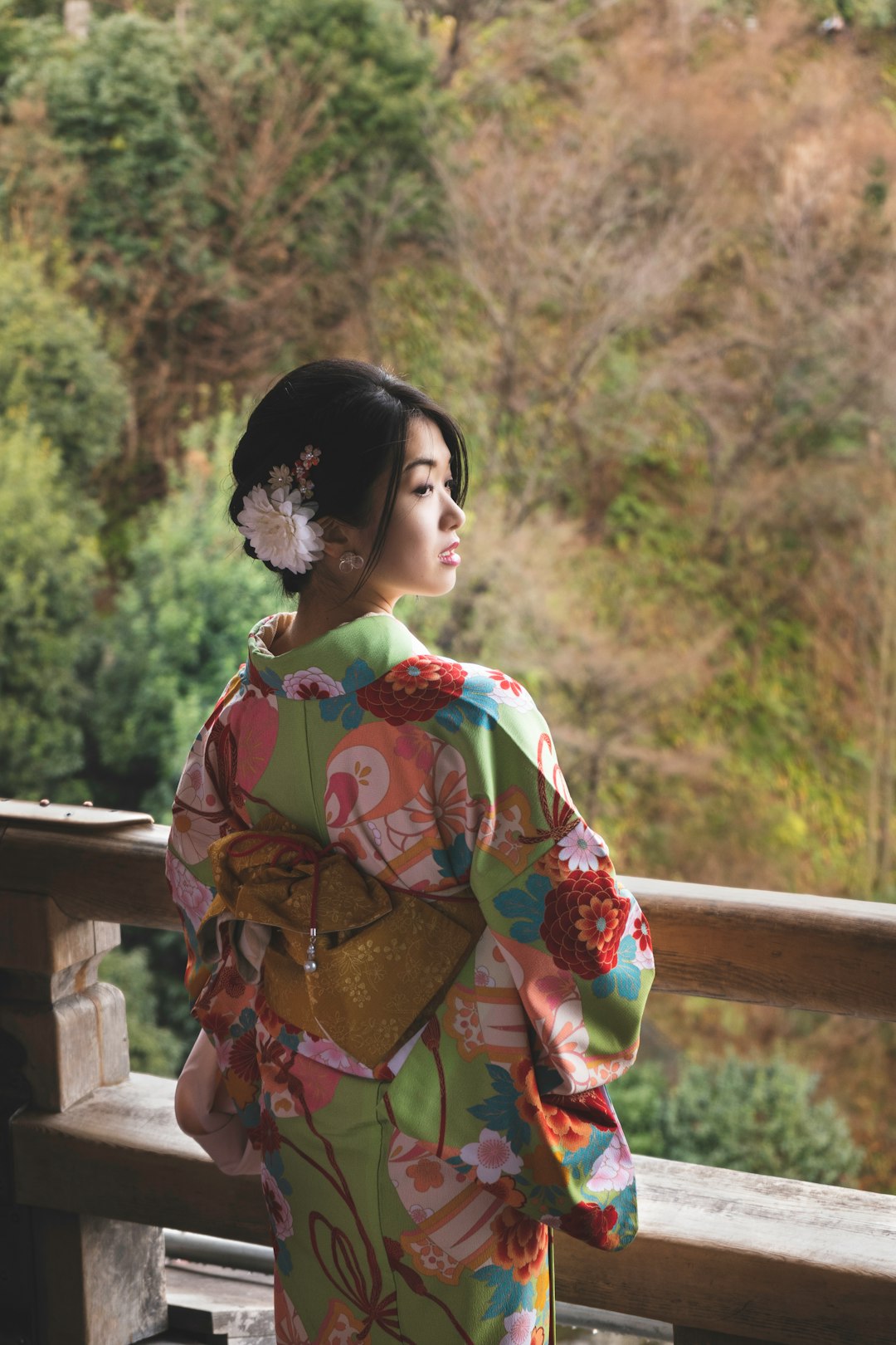woman in red and yellow floral kimono standing near brown wooden fence during daytime