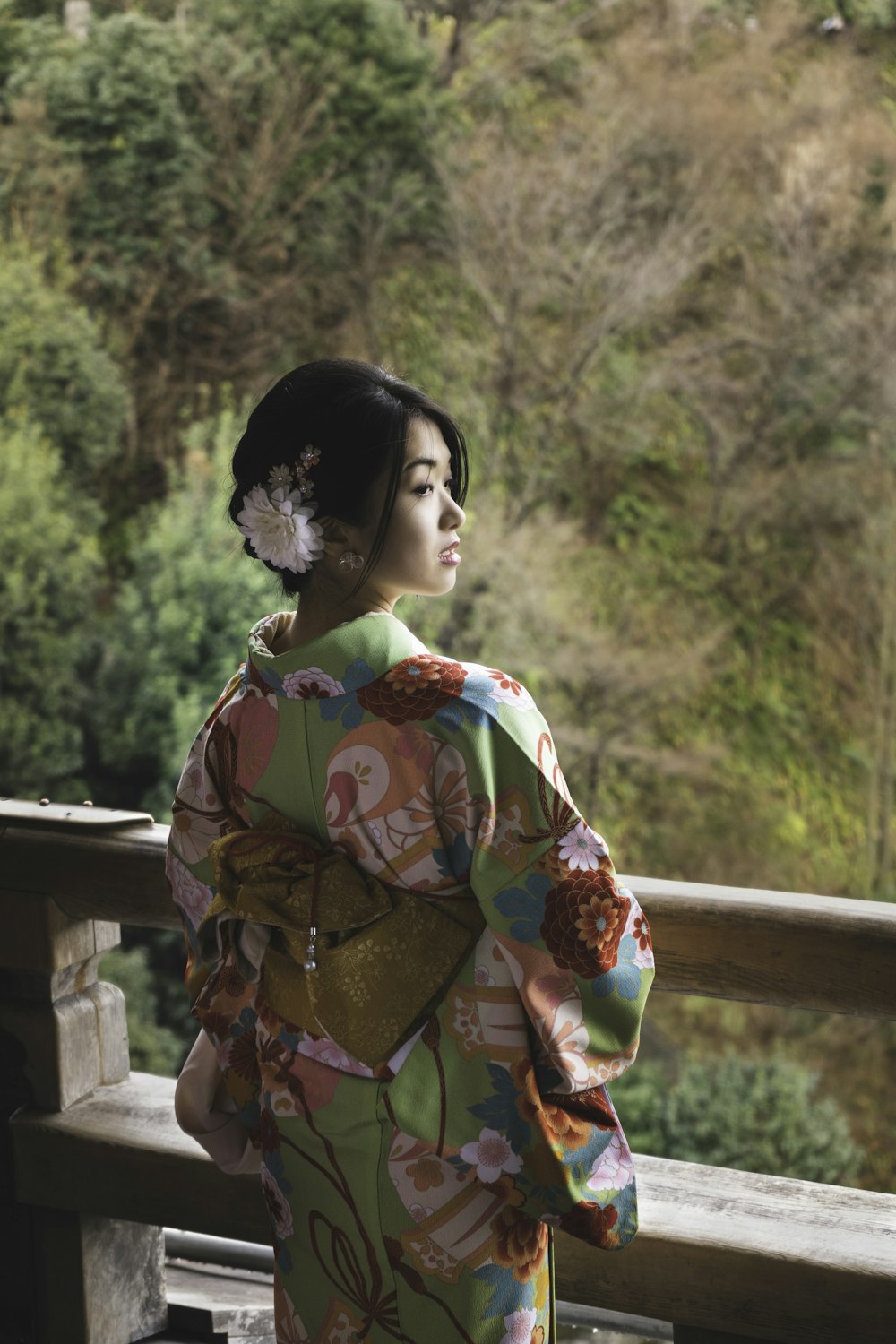 woman in red and yellow floral kimono standing near brown wooden fence during daytime