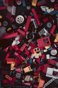 A chaotic pile of colorful LEGO pieces in various shapes and sizes, including red, yellow, blue, and black blocks as well as wheels and windows.