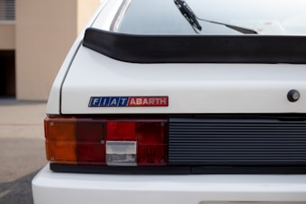The rear view of a white car displaying the FIAT and ABARTH logos. The image focuses on the tail light with a combination of orange, red, and white sections. A black spoiler runs along the top edge of the car's trunk.