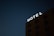 A dark night sky serves as the backdrop for a building with a brightly illuminated sign that reads 'HOTEL'. The building has multiple windows with balconies visible.