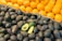 A display of fresh produce with a foreground of dark avocados, some whole and one cut in half revealing green interior, and a background of bright orange tangerines stacked in a neat arrangement.