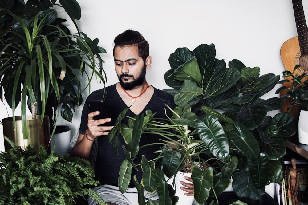 man in black polo shirt standing beside green plant