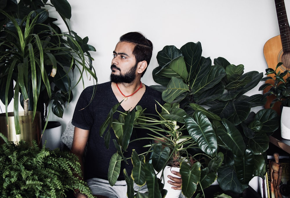 man in black crew neck t-shirt standing beside green plant