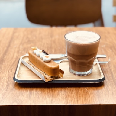 A steaming cup of coffee on a wooden table with a pastry.