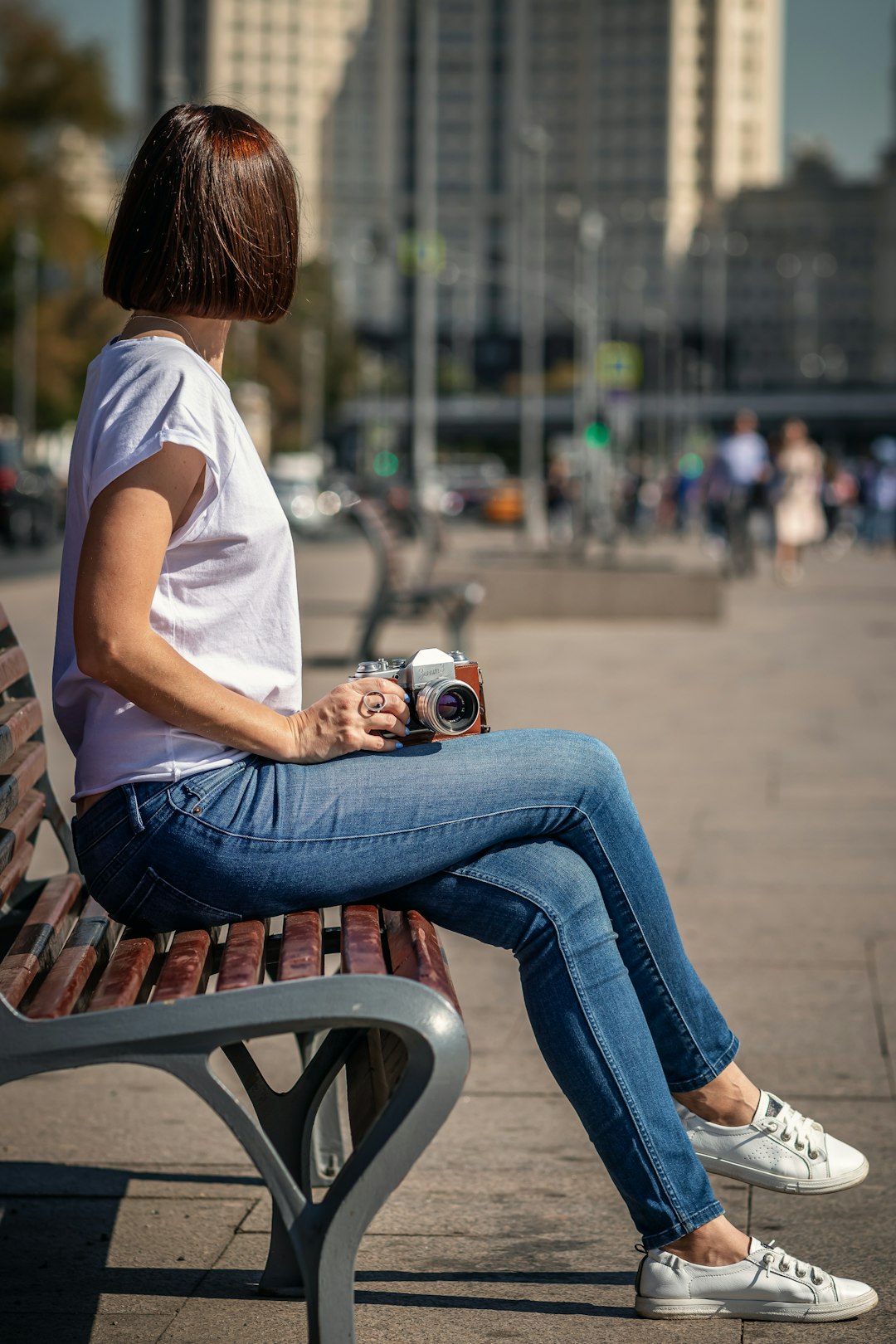 woman in white t-shirt and blue denim jeans sitting on brown wooden bench holding white