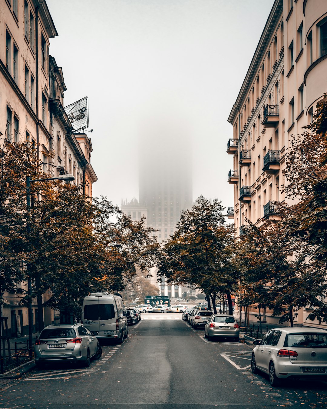 cars parked on side of the road in between high rise buildings during daytime