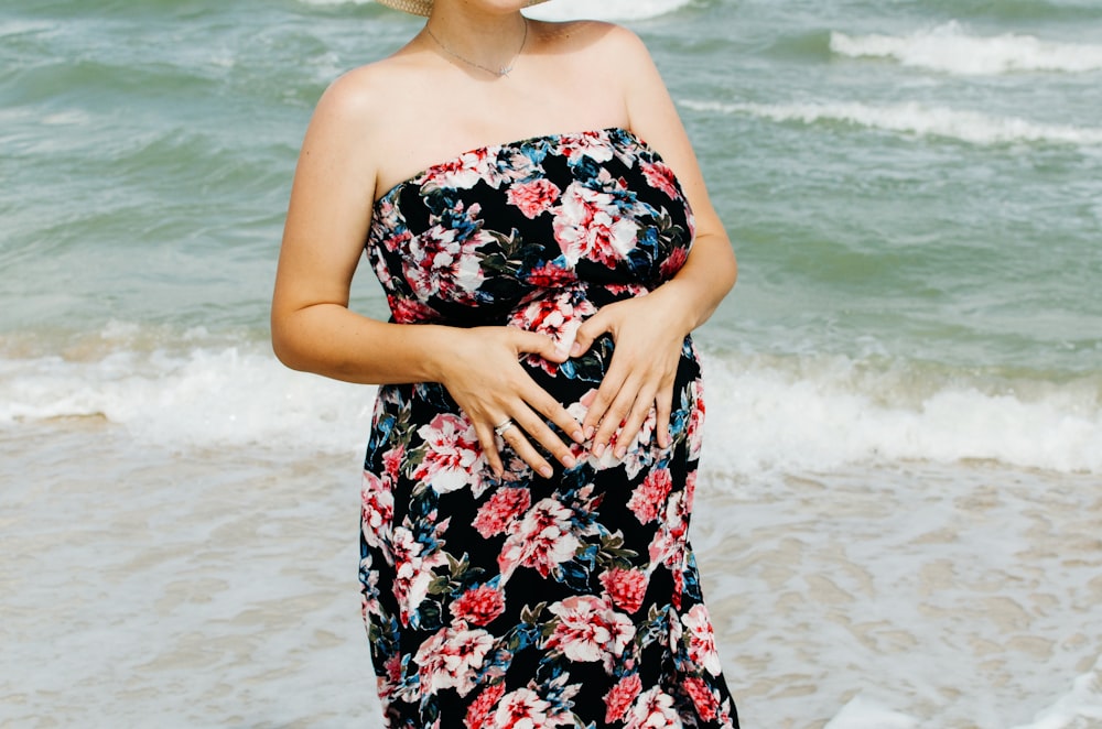 woman in black red and white floral tube dress standing on beach during daytime