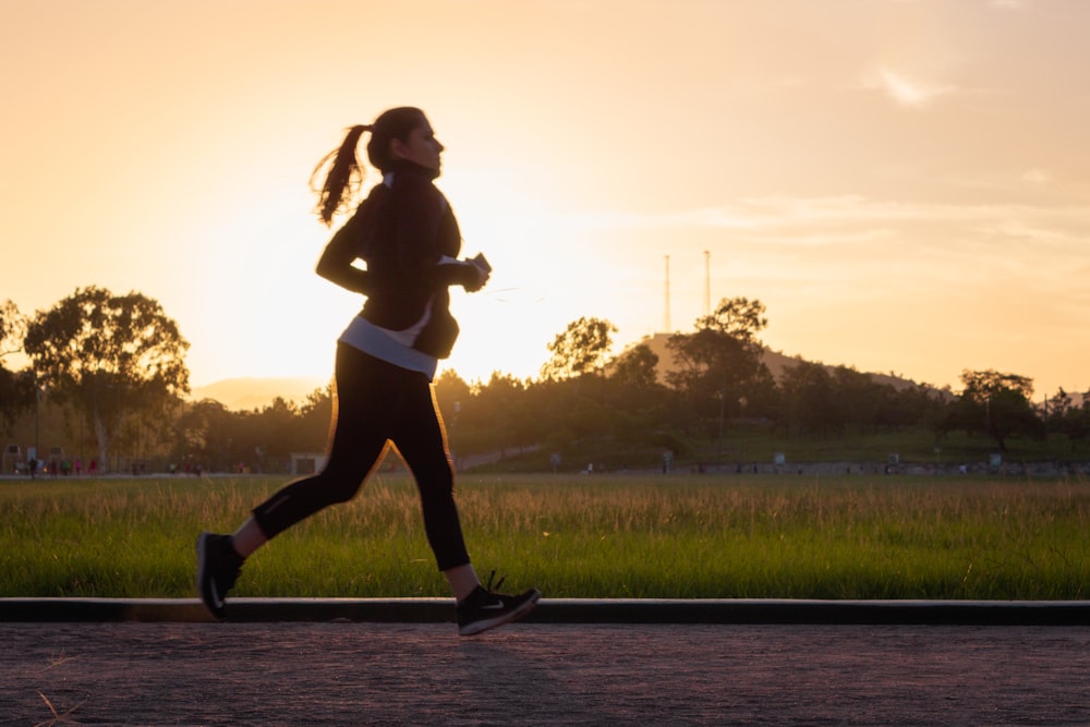 donna in reggiseno sportivo nero e pantaloni neri che corrono sull'acqua durante il tramonto