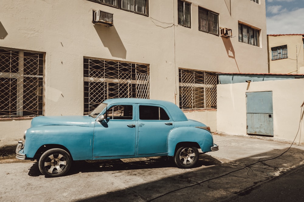 blue car parked beside white concrete building during daytime