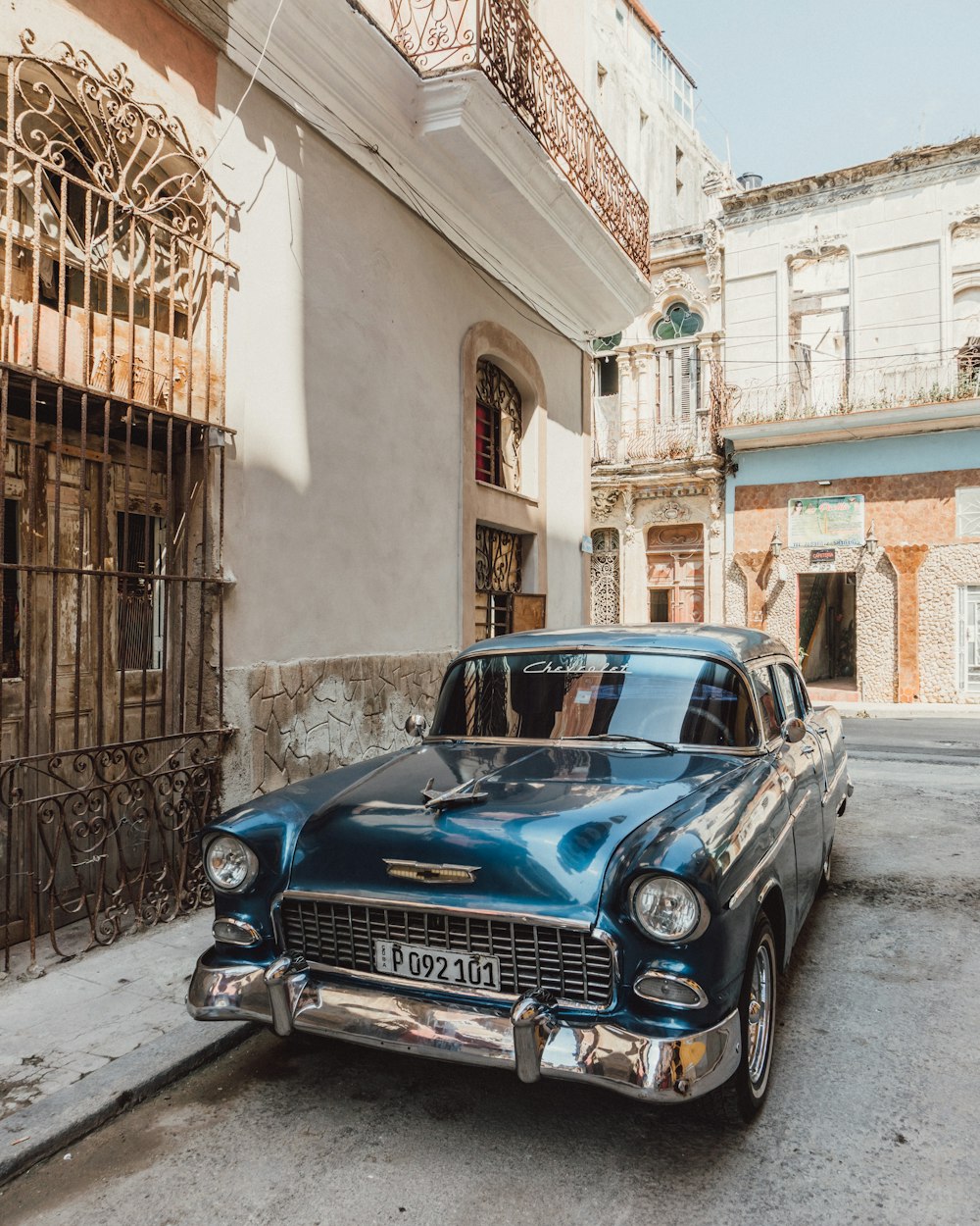 blue classic car parked beside brown concrete building during daytime