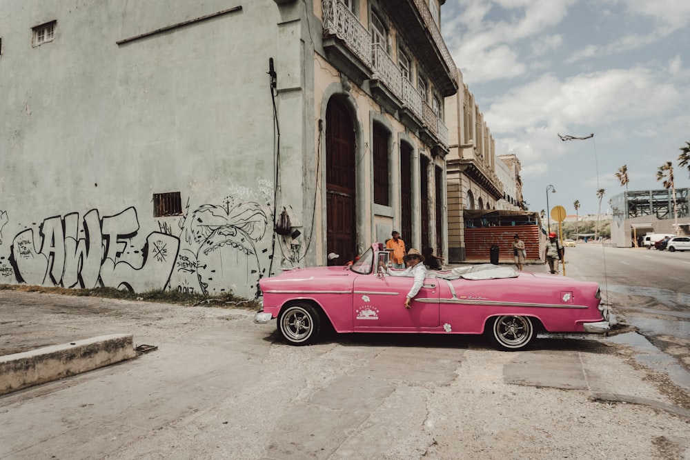 ピンクのコンバーチブル車は、日中に茶色のコンクリートの建物の横に駐車