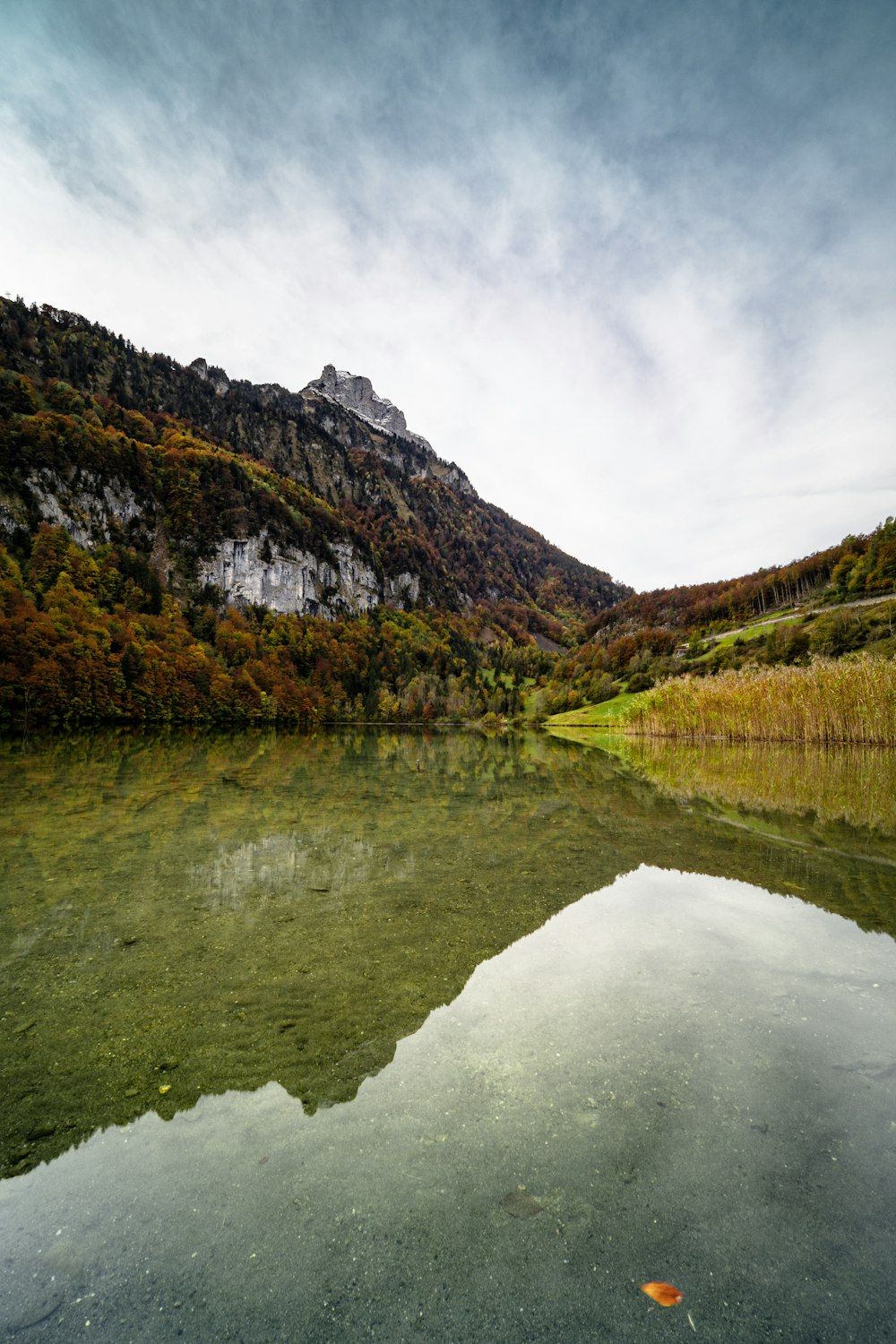 green and brown mountain beside lake under cloudy sky during daytime