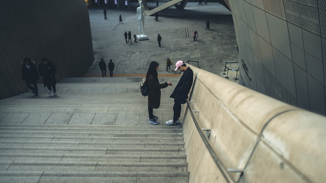 man in black jacket and blue denim jeans walking on gray concrete stairs