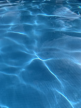 Clear water in a swimming pool displays gentle ripples and reflections of light. The surface shows various patterns created by the movement of water, with a serene and calming appearance.