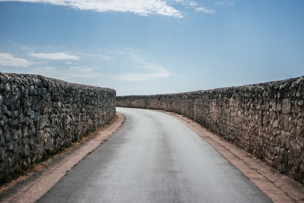 낮 동안 푸른 하늘 아래 회색 벽돌 벽 사이의 회색 아스팔트 도로