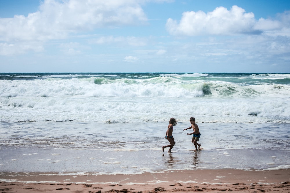 2 boys running on beach during daytime